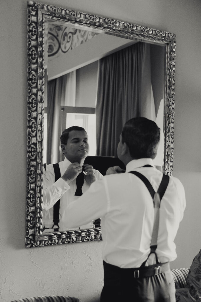 Groom getting ready photos in Peru, looking in the mirror as he ties his tie