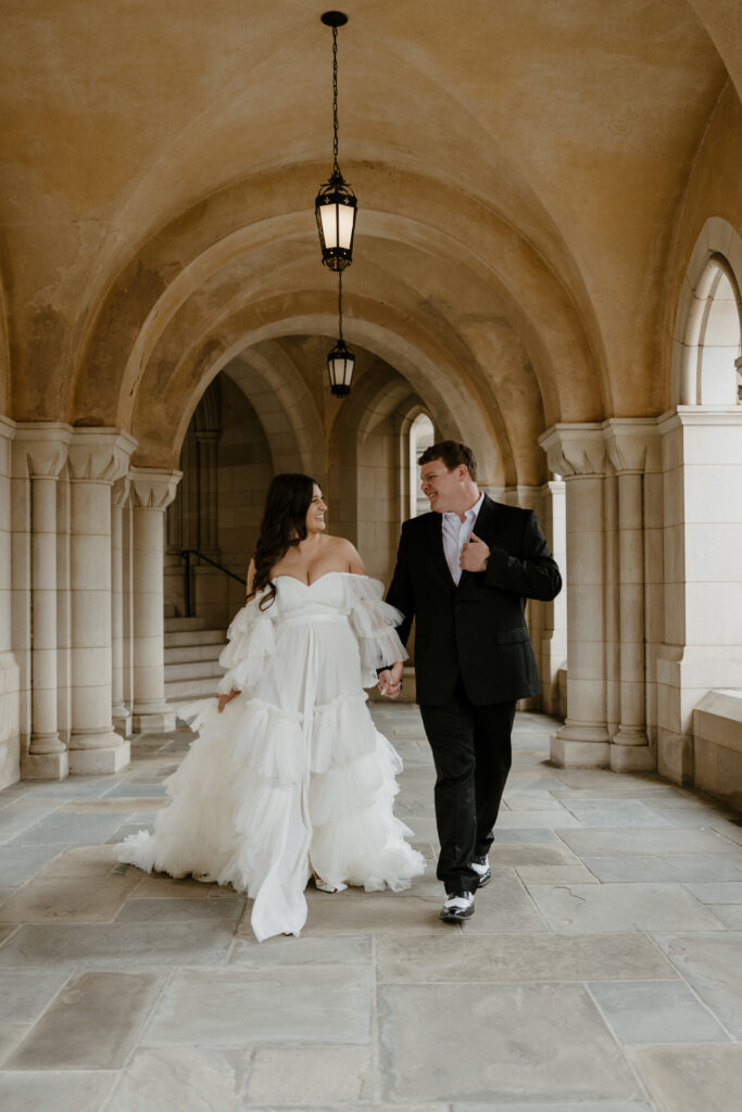 couple holding hands wearing a long white dress and a suit and tie at national cathedral walking down the hallway