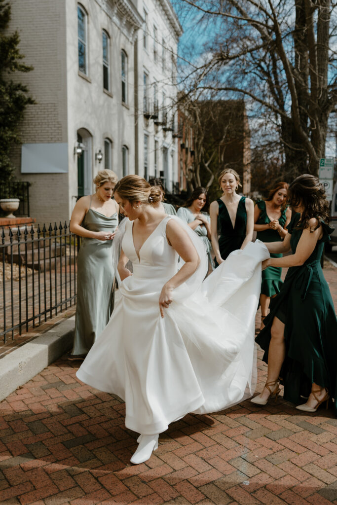 bridal party photo of bride walking while bridesmaids help with the back of her dress