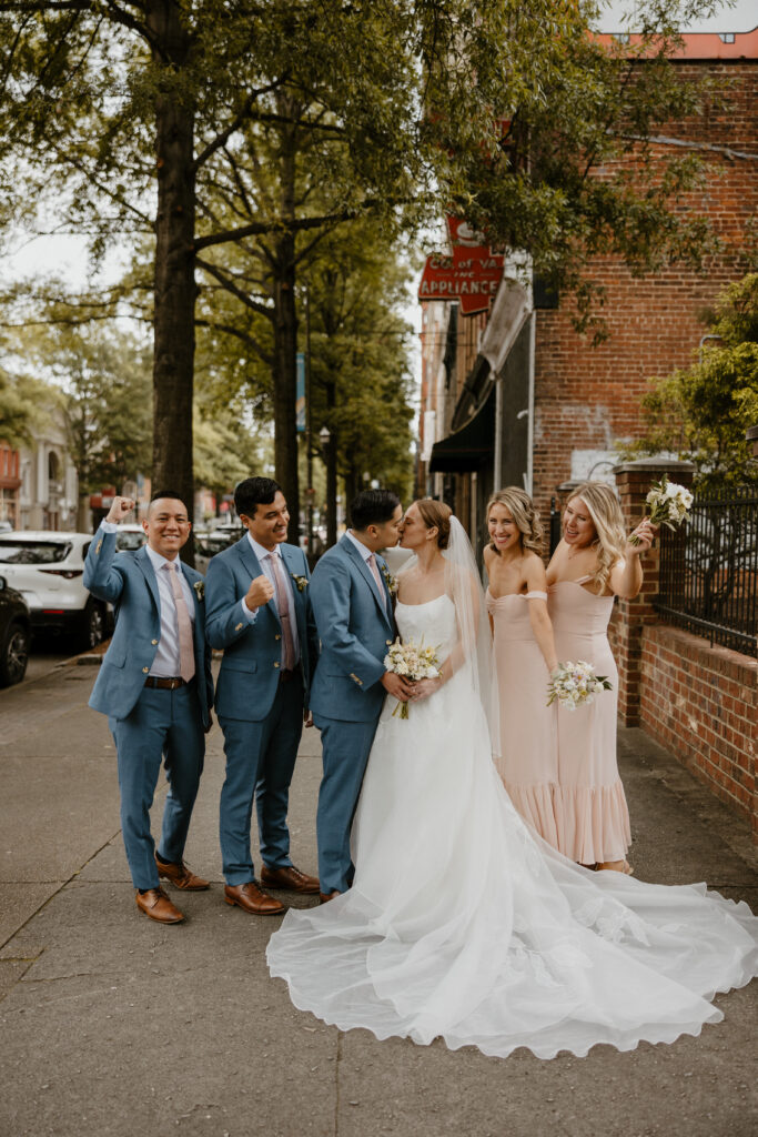 city wedding photo of bride and groom kissing surrounded by their bridal party