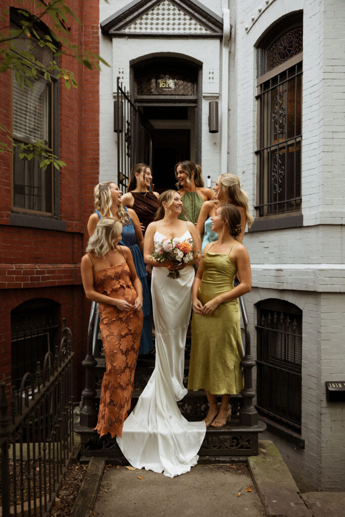 bridal party photo of bride holding her bouquet and bridesmaids standing around her in different color dresses