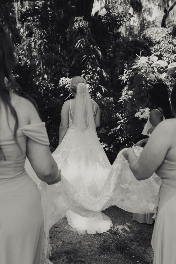 wedding detail photo of bridesmaids helping bride by carrying the train of her dress