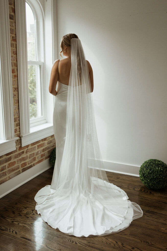 bridal portrait of bride standing in her wedding dress and veil looking out the window