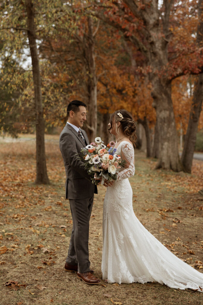 first look photo of bride and groom surrounded by fall foliage and bride holding her beautiful big colorful bouquet
