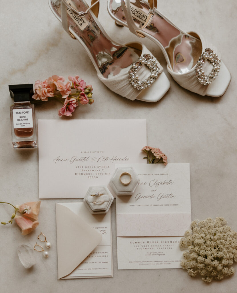 a wedding detail photo of a flatlay including wedding perfume, wedding flowers, wedding invitation, wedding rings, wedding earrings and wedding shoes